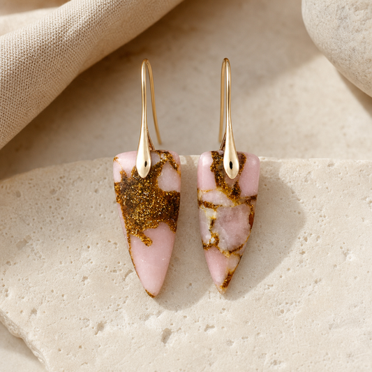 Gold pink natural stone geometric earrings on a warm stone surface.