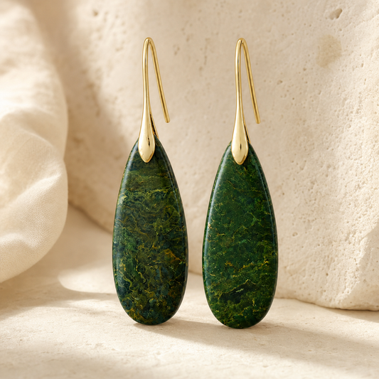 Gold green natural stone waterdrop earrings on a warm stone surface.